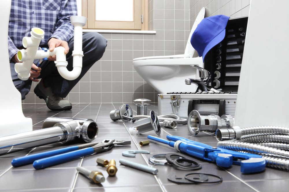 Plumber installing bathroom fixtures with full tool kit on floor