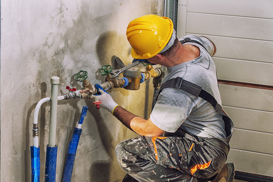 Plumber with hard hat working on wall-mounted pipe valves