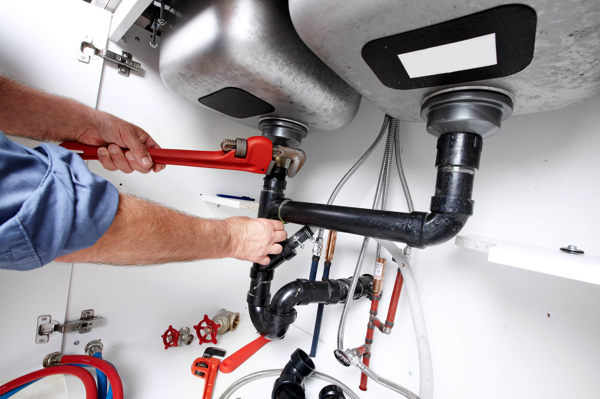 Plumber repairing pipes under kitchen sink with red wrench