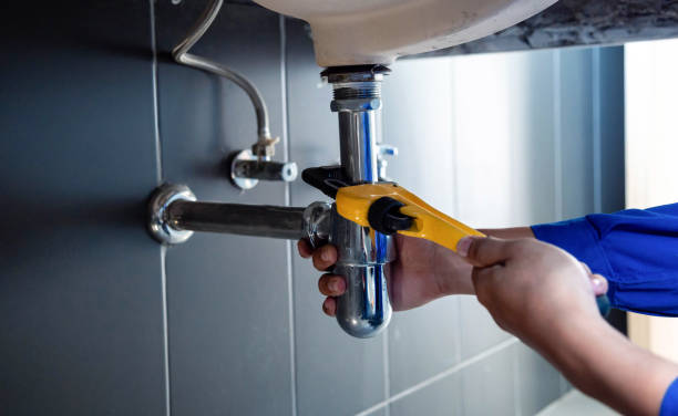 Plumber tightening bathroom sink pipe with yellow wrench